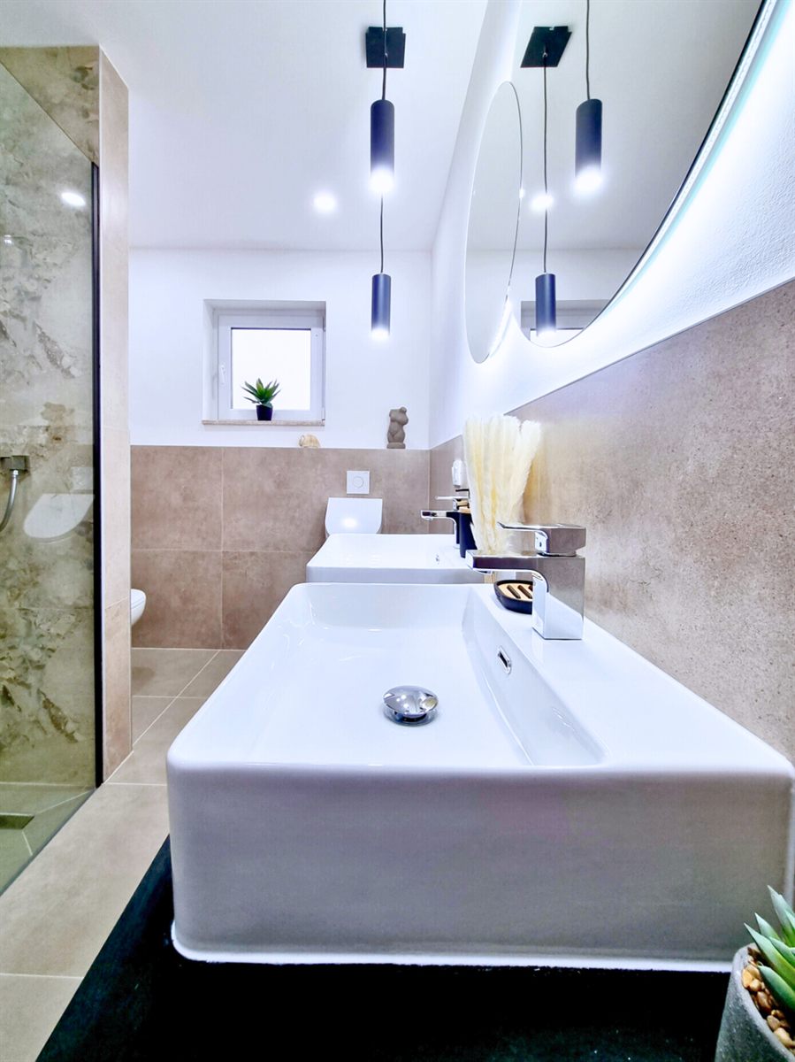 Waschbecken-Nahaufnahme mit Pendelleuchten und LED-Spiegel, Badezimmer Ferienhaus Biograci